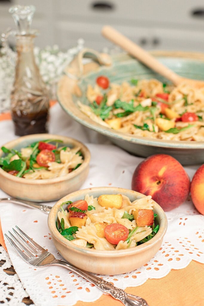 Peach caprese pasta salad served in small bowls with fresh peaches and a serving bowl in the background