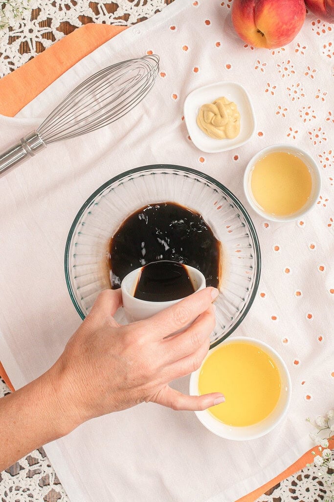 Whisking balsamic vinaigrette in a glass bowl with mustard and peach juice for pasta salad dressing