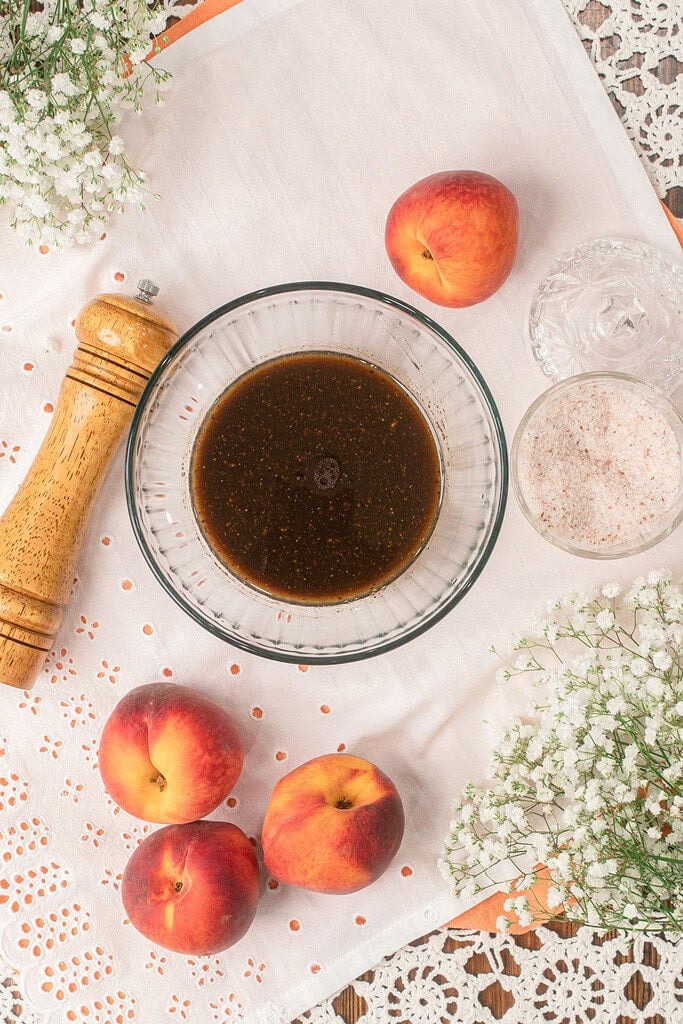 Overhead view of whisked balsamic vinaigrette in a glass bowl surrounded by fresh peaches and salt