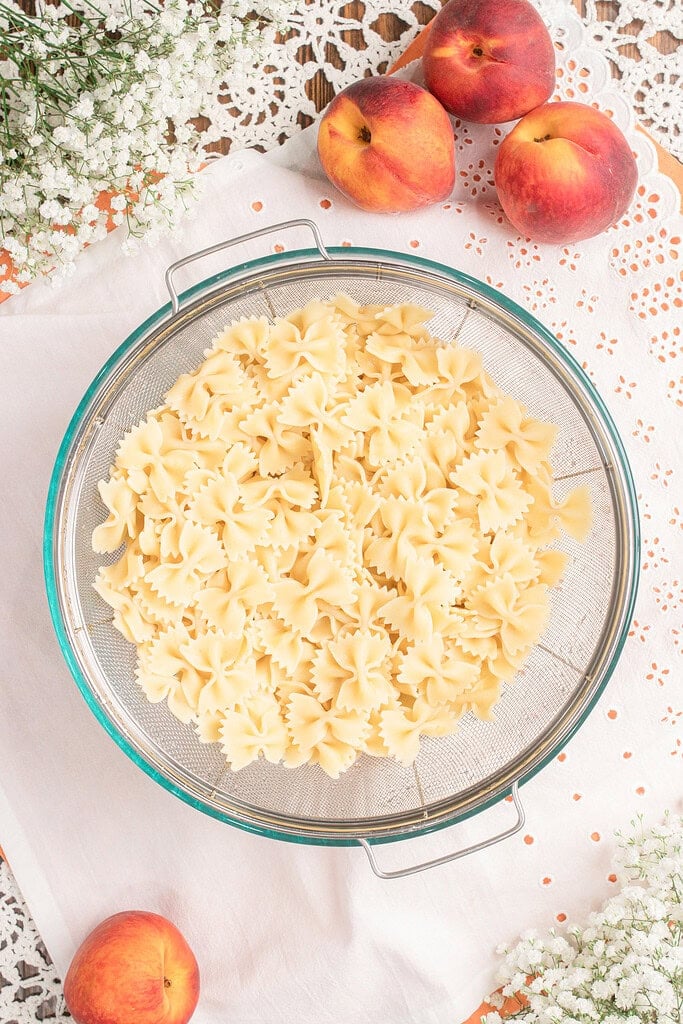 Cooked bowtie pasta draining in a colander with fresh peaches nearby