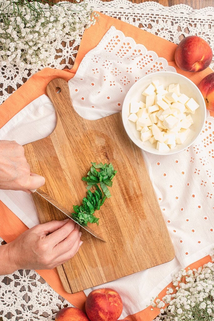 Slicing fresh basil on a wooden cutting board next to a bowl of cubed mozzarella