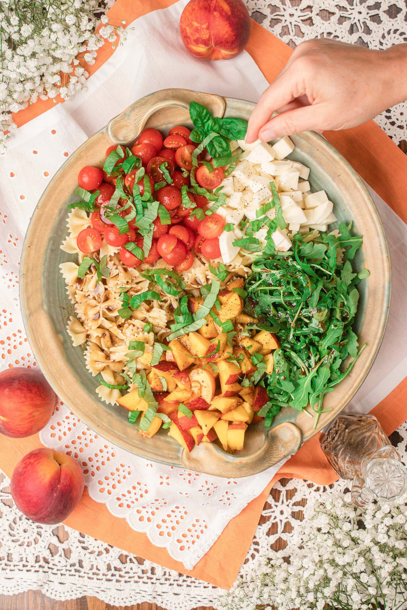 Adding fresh mozzarella by hand to peach caprese pasta salad topped with basil and balsamic dressing