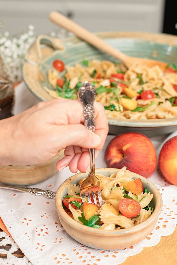 Forkful of peach caprese pasta salad with cherry tomatoes and peach chunks in a small bowl