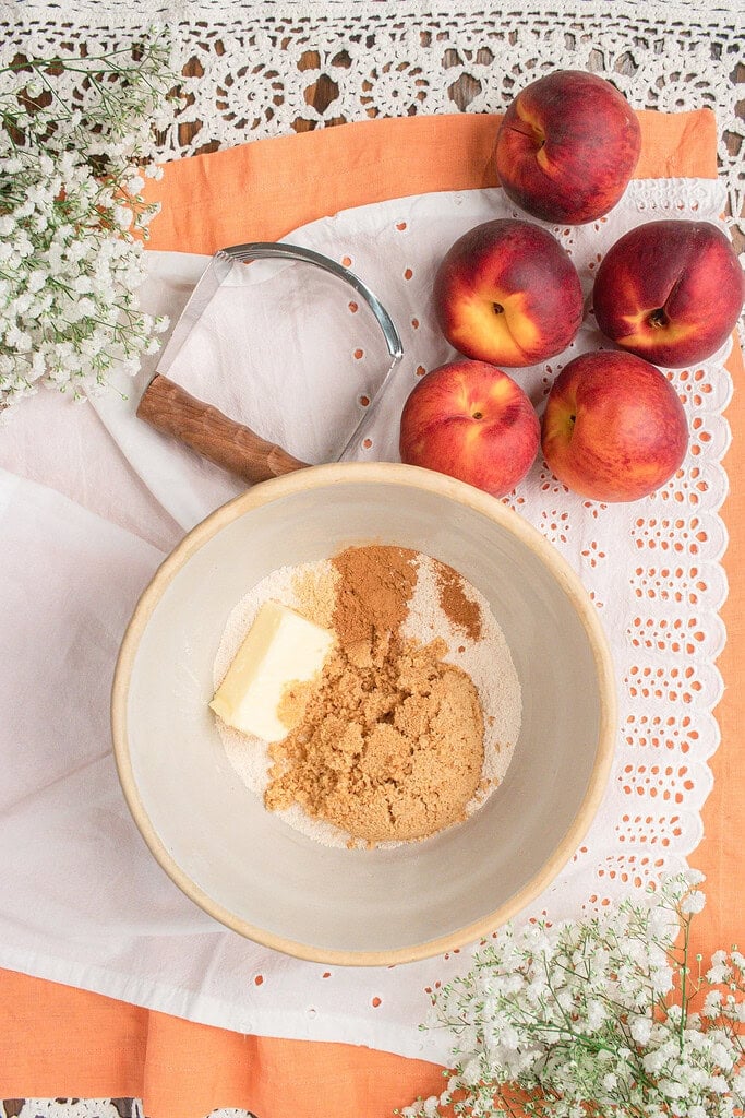 Ingredients for fresh milled flour peach crisp topping including freshly milled flour, butter, brown sugar, cinnamon, ginger, and fresh peaches in a mixing bowl.