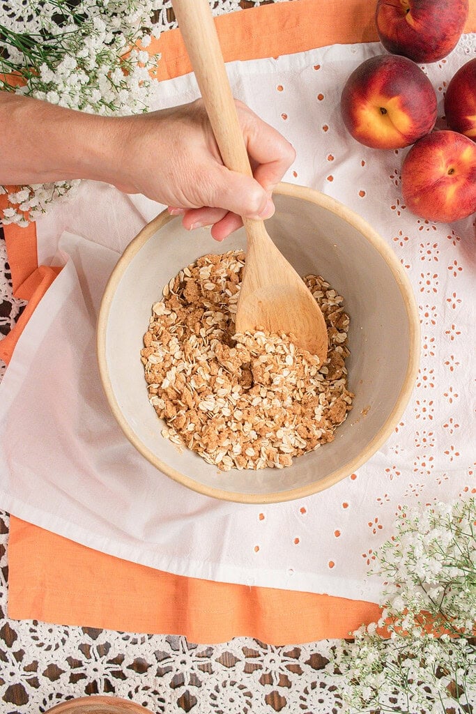 Stirring rolled oats into fresh milled flour crisp topping to make a buttery cinnamon oat topping for homemade peach crisp.
