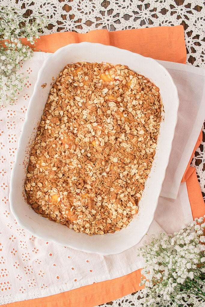 baked homemade peach crisp topped with fresh milled flour oat crumble before baking until golden brown.