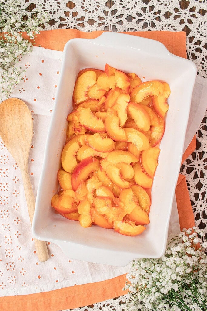 Fresh sliced peaches arranged in a baking dish before adding the fresh milled flour crumble topping for homemade peach crumble.
