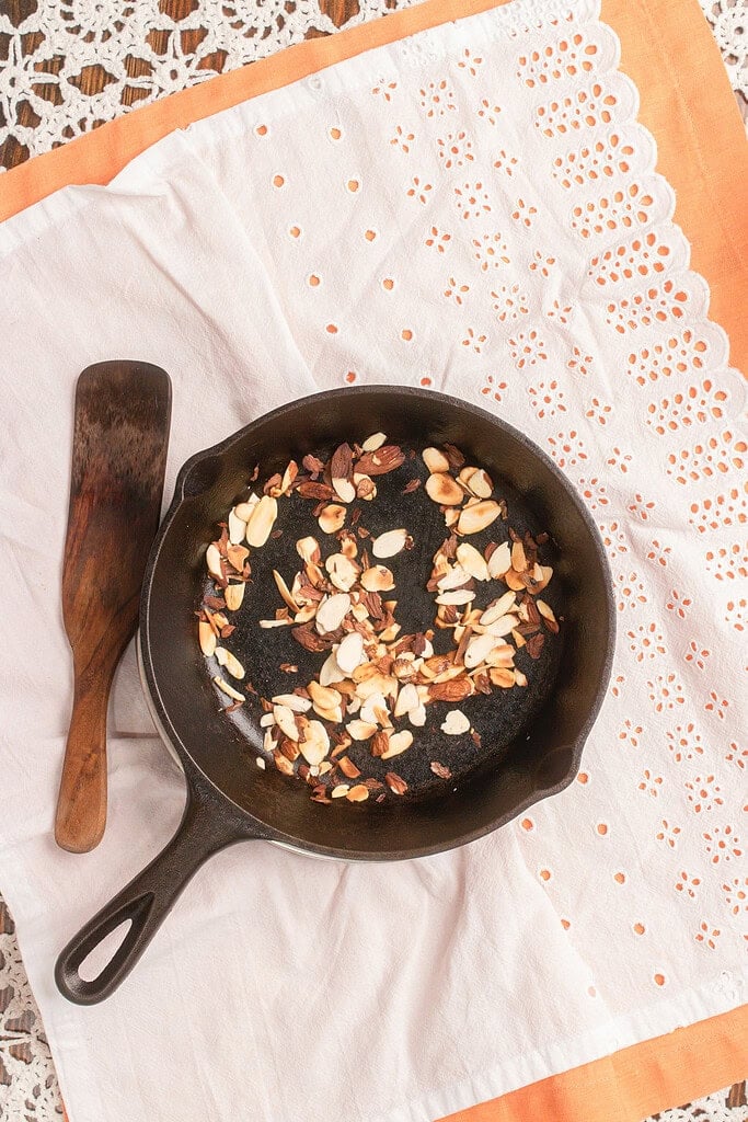 Toasting sliced almonds in a cast iron skillet to make crunchy topping for homemade peach farro salad.