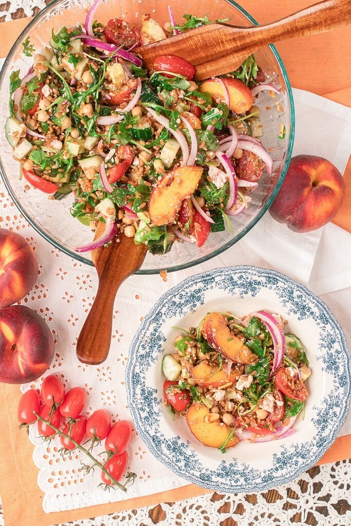 Large bowl of homemade peach farro salad tossed with fresh peaches, chickpeas, arugula, cucumber, cherry tomatoes, red onion, feta, and toasted almonds.