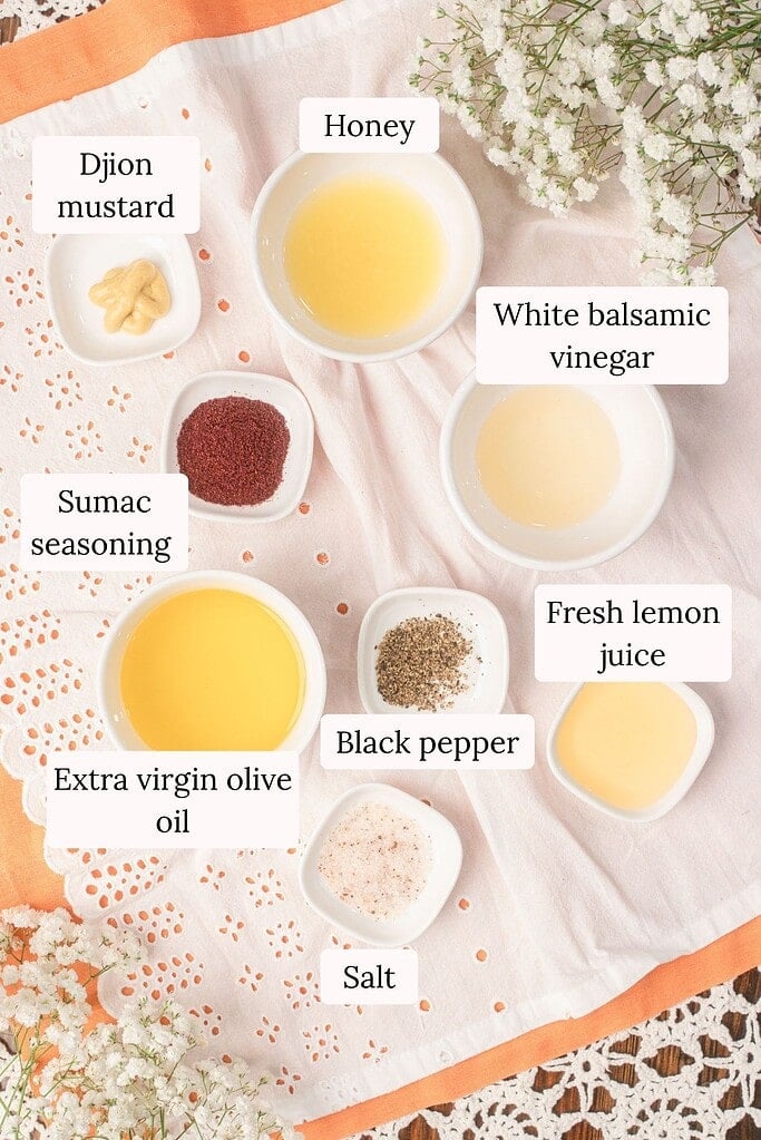 Ingredients for homemade honey lemon vinaigrette for peach farro salad including extra virgin olive oil, white balsamic vinegar, fresh lemon juice, honey, Dijon mustard, sumac, black pepper, and salt arranged overhead.