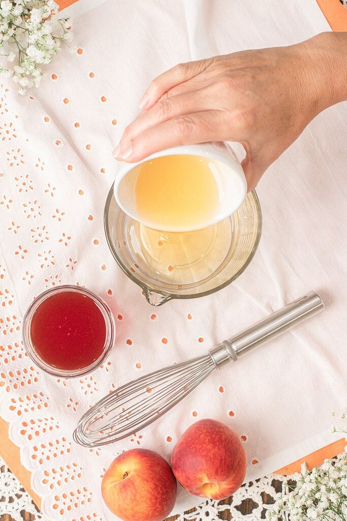 Pouring freshly squeezed lemon juice into a measuring cup while preparing homemade peach lemonade with peach simple syrup.