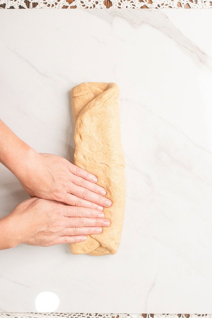 Fresh milled flour dough rolled into a tight log shape on a marble countertop, ready to be sealed
