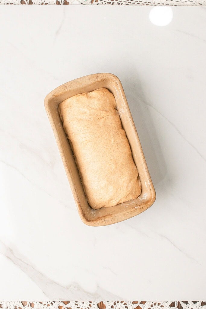 Shaped Fresh Milled Flour Sandwich Bread dough resting in a greased loaf pan on a marble countertop before rising