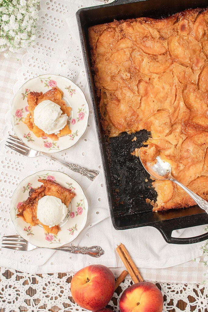 Overhead view of homemade sourdough peach cobbler baked in a cast iron baking dish with two servings topped with vanilla ice cream.