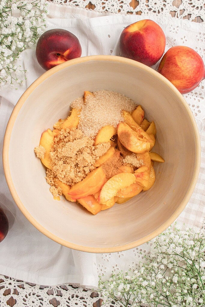 Fresh sliced peaches with organic cane sugar, brown sugar, cinnamon, and spices in a mixing bowl before making sourdough peach cobbler with fresh milled flour.