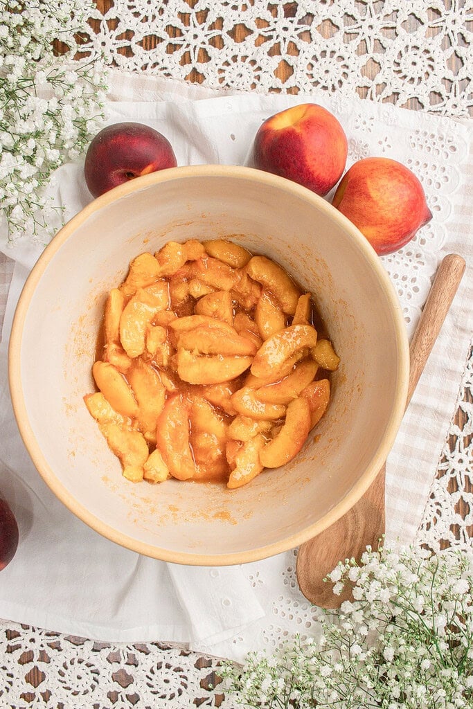 Fresh peaches tossed with sugar and cinnamon until evenly coated for homemade sourdough peach cobbler with fresh milled flour.
