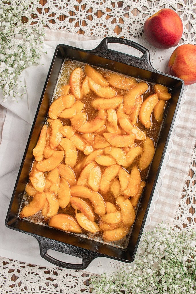Fresh peach filling arranged in a cast iron baking dish before adding the sourdough fresh milled flour cobbler batter.