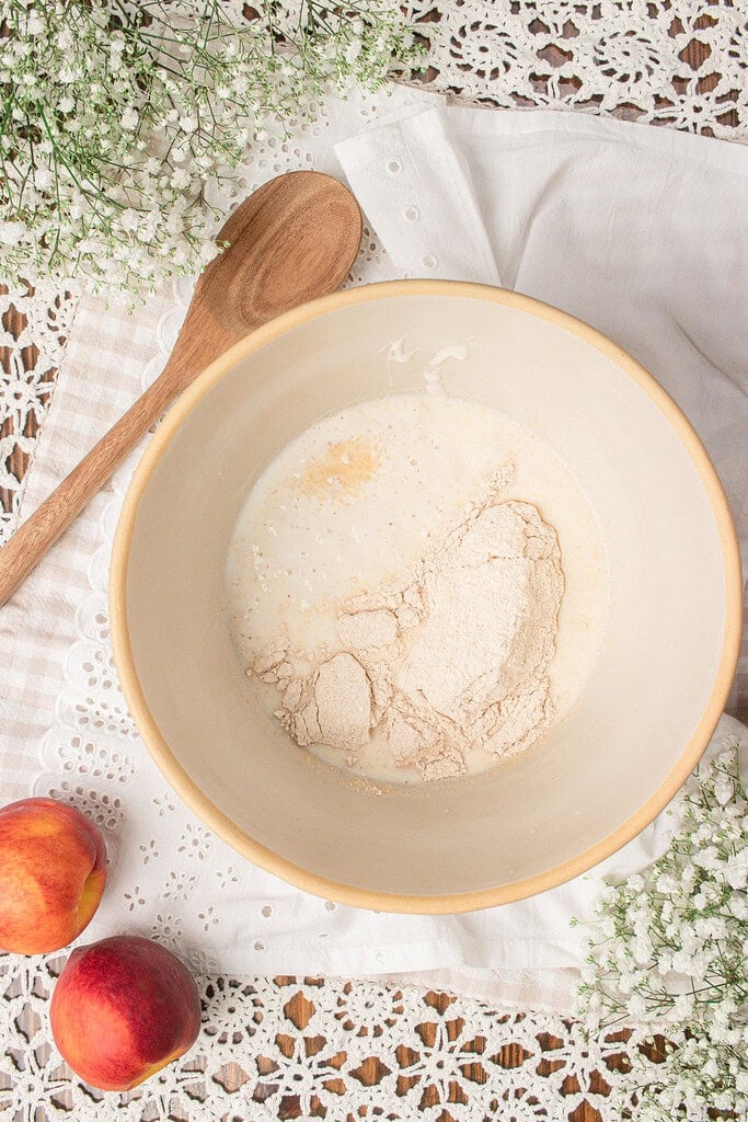 Fresh milled flour and sourdough starter combined with milk in a mixing bowl to make homemade sourdough peach cobbler batter.