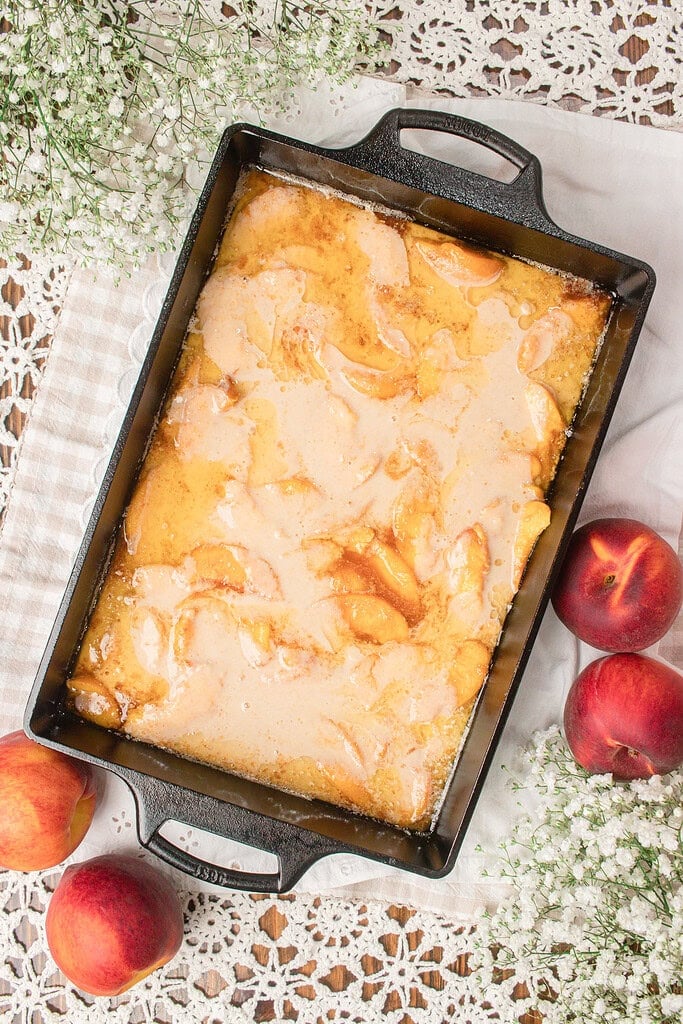 Sourdough fresh milled flour cobbler batter poured over sliced peaches in a cast iron baking dish before baking.