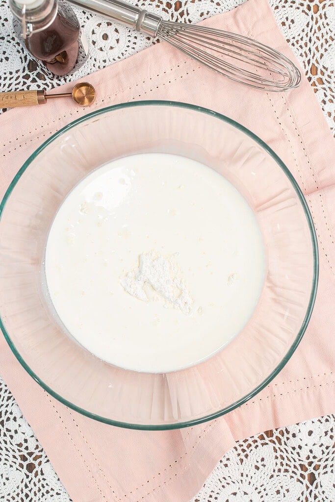 Heavy whipping cream in a glass bowl with the cornstarch and powdered sugar mixture added on top, ready to be whisked together before whipping
