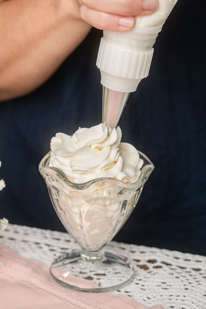 Close up of stabilized whipped cream being piped into a glass dessert dish using a star piping tip, building tall rosette swirls