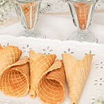 Homemade fresh milled flour waffle cones filled with scoops of vanilla ice cream in vintage glass dessert cups, with additional crisp waffle cones arranged on a white serving tray.