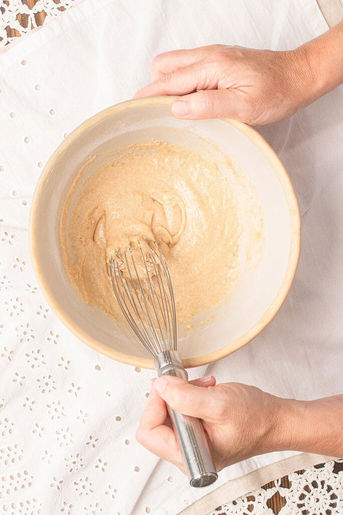 Hands whisking homemade waffle cone batter made with fresh milled flour in a large mixing bowl before cooking the waffle cones.