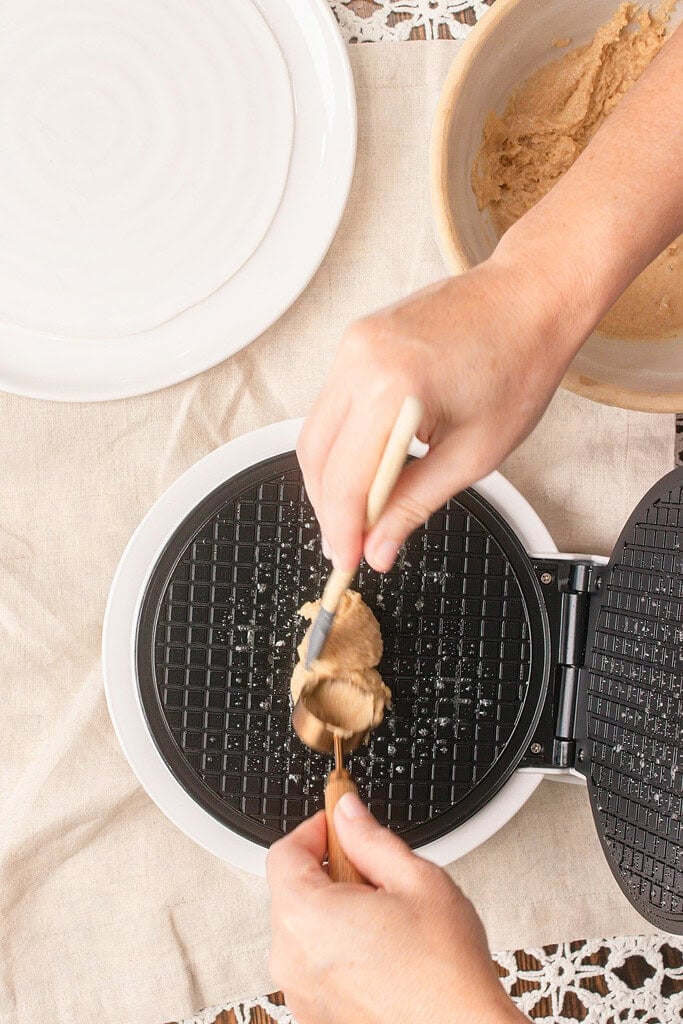 Spooning fresh milled flour waffle cone batter onto a preheated waffle cone maker before spreading the batter into an even layer.