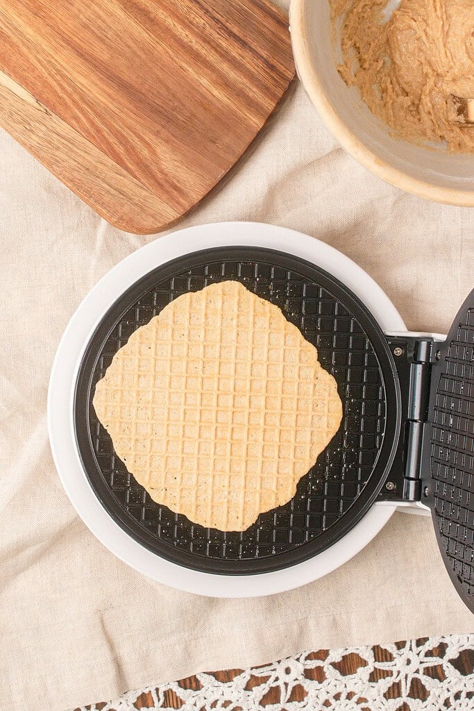 Freshly cooked homemade waffle cone made with fresh milled flour baking on an open waffle cone maker until lightly golden.