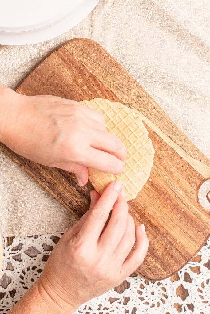 Hands rolling a warm homemade waffle cone made with fresh milled flour around a cone mold while it is still soft and pliable.