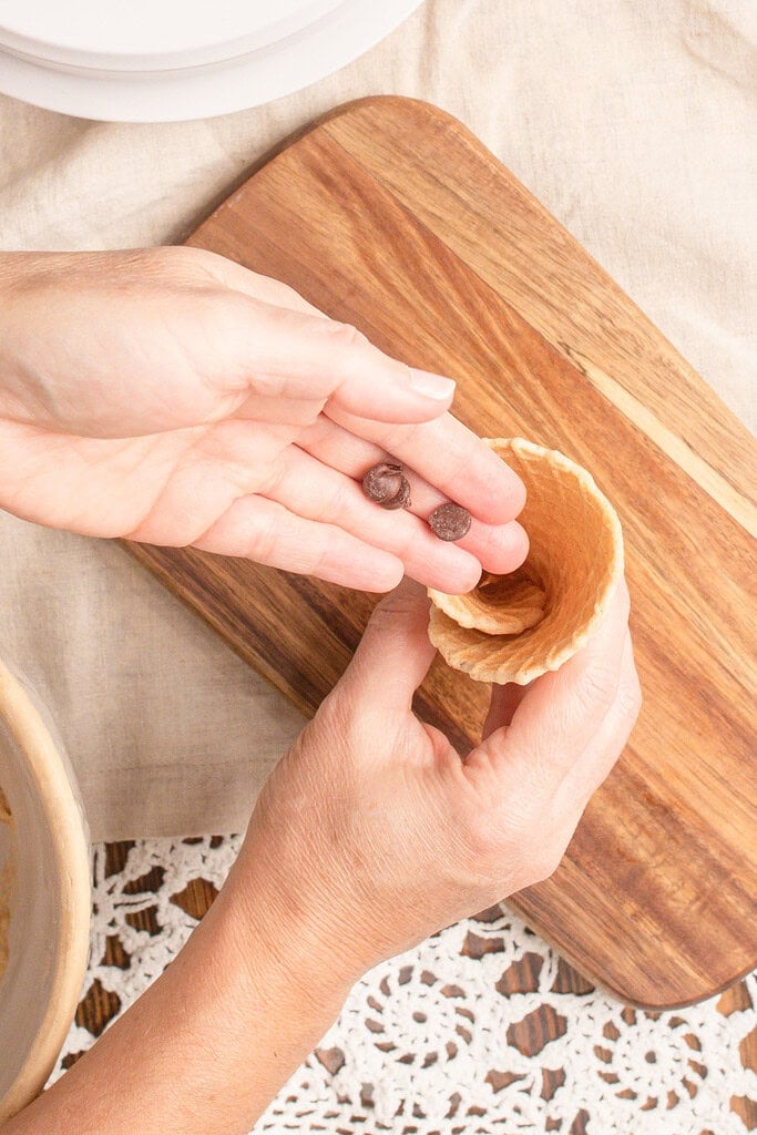 Adding chocolate chips to the bottom of a freshly rolled homemade waffle cone made with fresh milled flour to create a chocolate-lined ice cream cone.