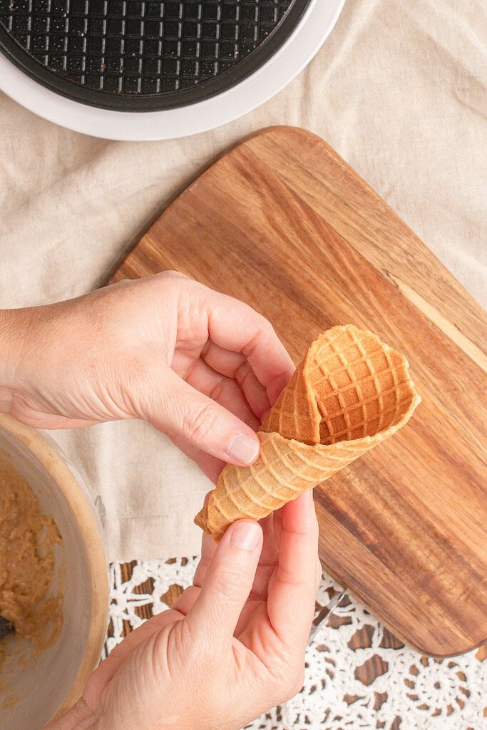 Hands holding a freshly rolled homemade waffle cone made with fresh milled flour, showing its crisp golden texture and classic waffle pattern.