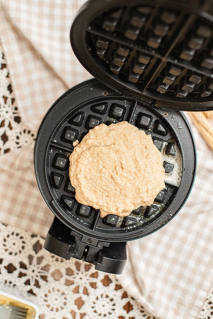 Overhead view of waffle batter made with freshly milled flour spooned onto an open waffle iron, ready to close and cook.