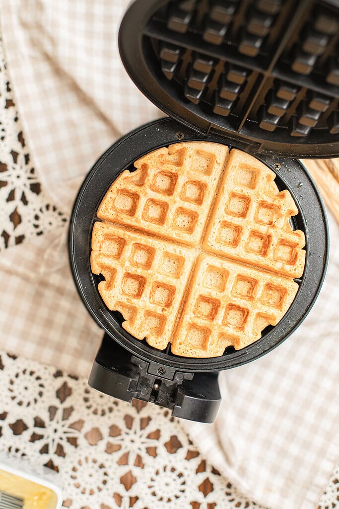 Overhead view of a golden brown waffle made with freshly milled flour fresh off the iron, still resting on the open waffle maker.