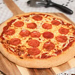 A whole baked pepperoni pizza on freshly milled flour dough, set on a wooden board next to a pizza cutter