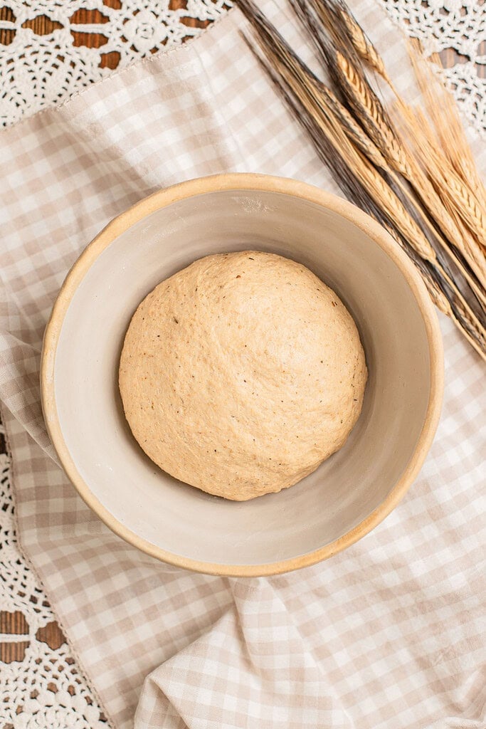 A smooth, risen ball of freshly milled flour pizza dough in a bowl beside dried wheat stalks