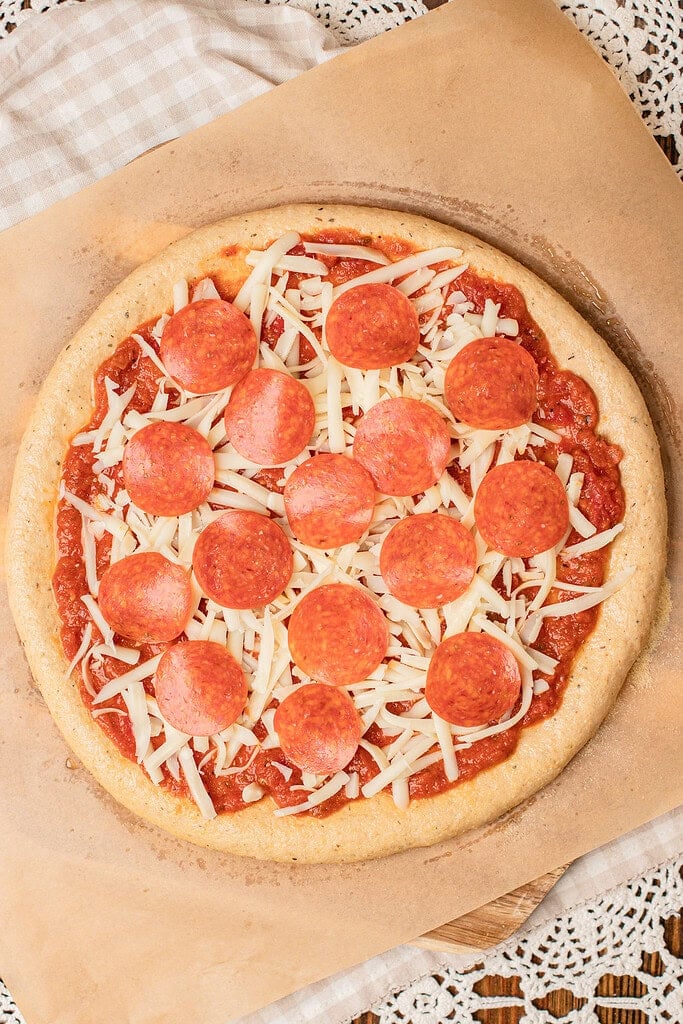 An unbaked pizza fully topped with sauce, cheese, and pepperoni on freshly milled flour dough