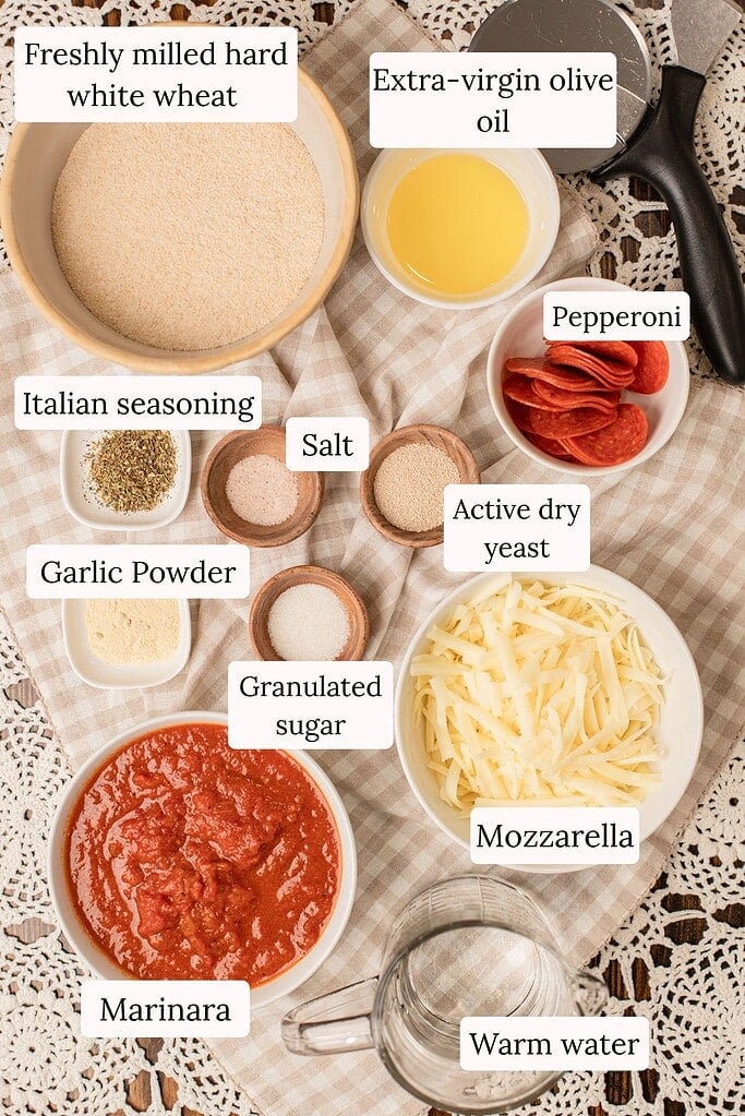 Freshly milled flour, olive oil, pepperoni, shredded mozzarella, marinara, yeast, and seasonings arranged in bowls for homemade pizza dough