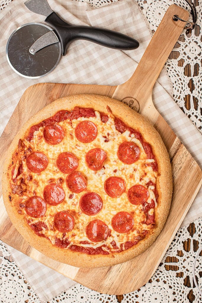 A baked freshly milled flour pizza dough crust with melted cheese and pepperoni, resting on a wooden pizza peel