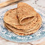 A stack of folded tortillas made with freshly milled flour piled on a blue floral plate, char marks visible on top
