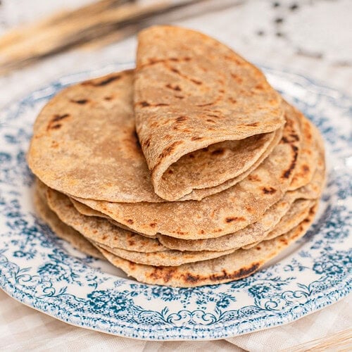 A stack of folded tortillas made with freshly milled flour piled on a blue floral plate, char marks visible on top