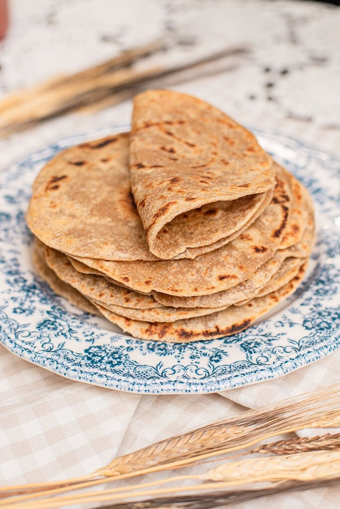 A stack of folded tortillas made with freshly milled flour piled on a blue floral plate, char marks visible on top