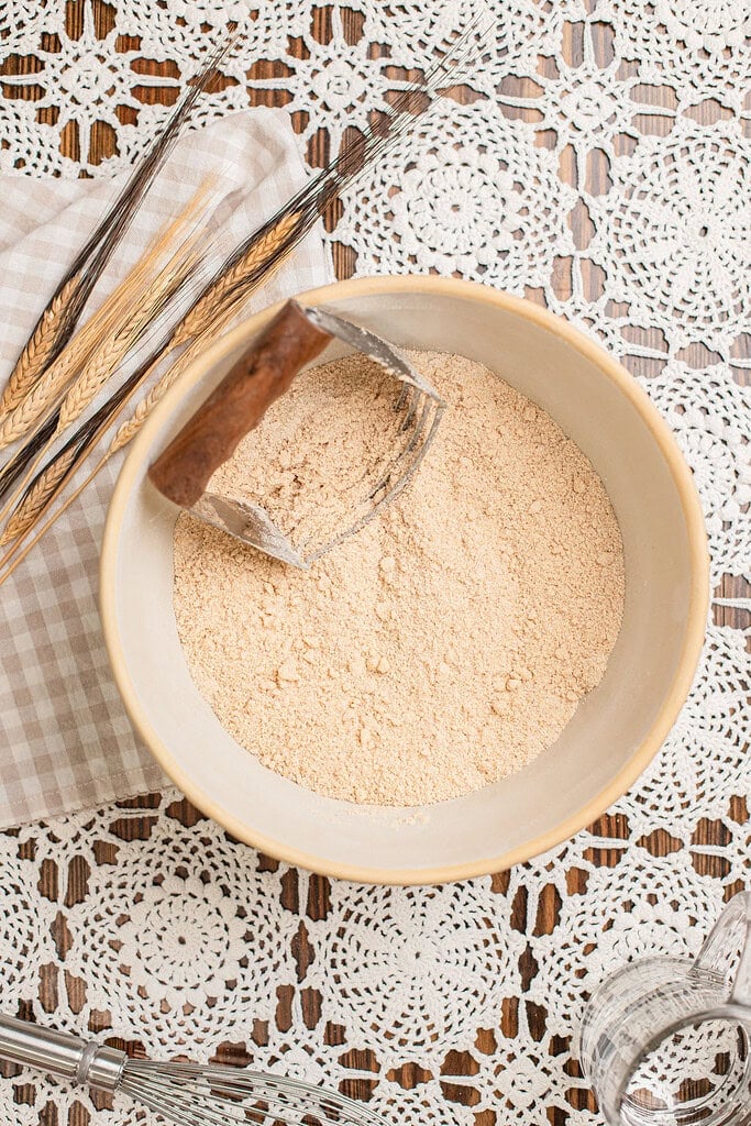 Freshly milled flour scooped with a dough cutter in a bowl, wheat stalks laid alongside