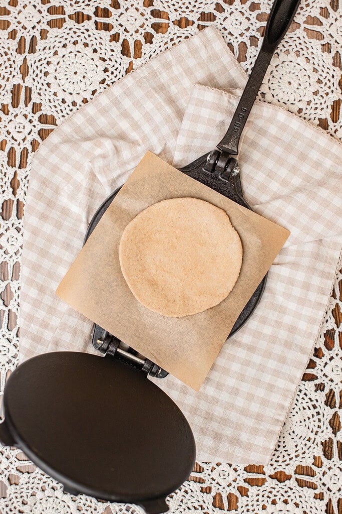 A rolled round of freshly milled flour tortilla dough resting on parchment paper beside a tortilla press