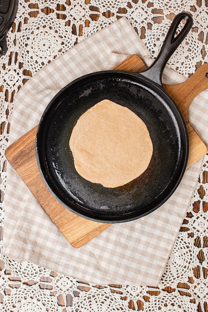 A tortilla made with freshly milled flour cooking in a cast iron skillet, still pale before browning