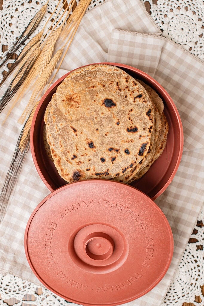A stack of finished tortillas made with freshly milled flour inside a round tortilla warmer, lid propped open