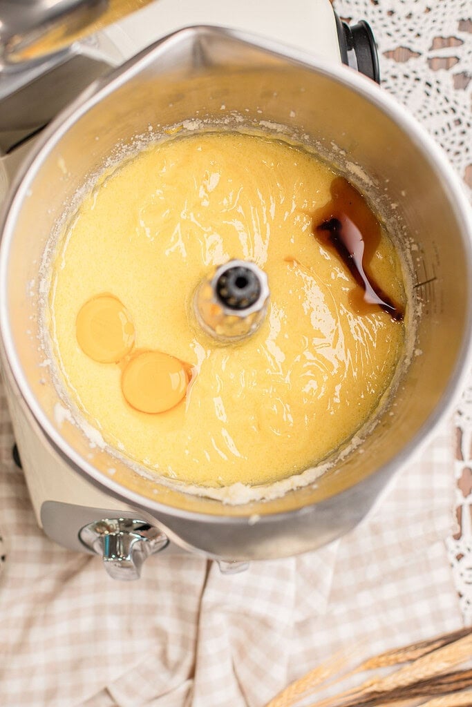 Cake batter in a stand mixer bowl with two egg yolks and a swirl of vanilla extract poured in, not yet mixed