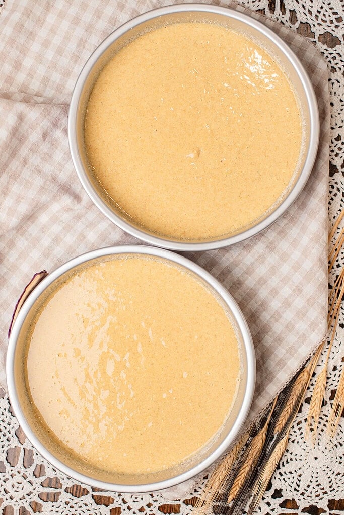 Two round cake pans filled with batter for freshly milled flour yellow cake, set on a checked cloth before baking