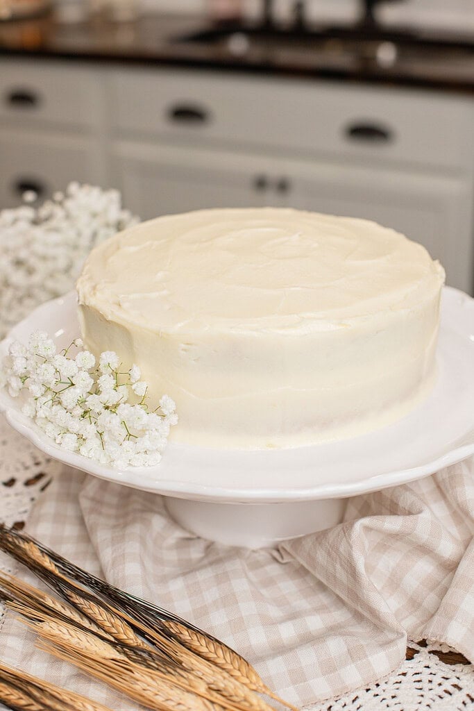A frosted freshly milled flour yellow cake on a white cake stand, decorated with baby's breath and wheat stalks
